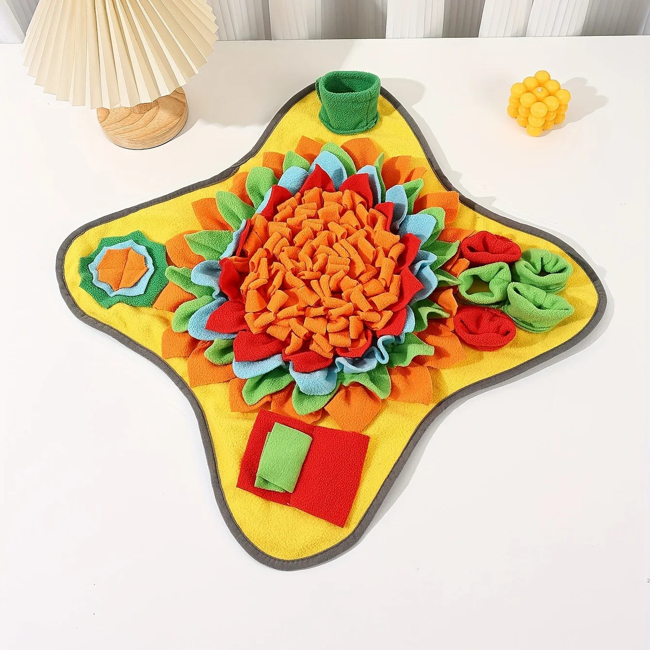 Colorful flower-shaped mat on a white surface with a lamp in the background